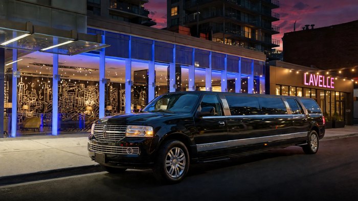 Black Lincoln Navigator stretch limousine outside an illuminated downtown venue at twilight