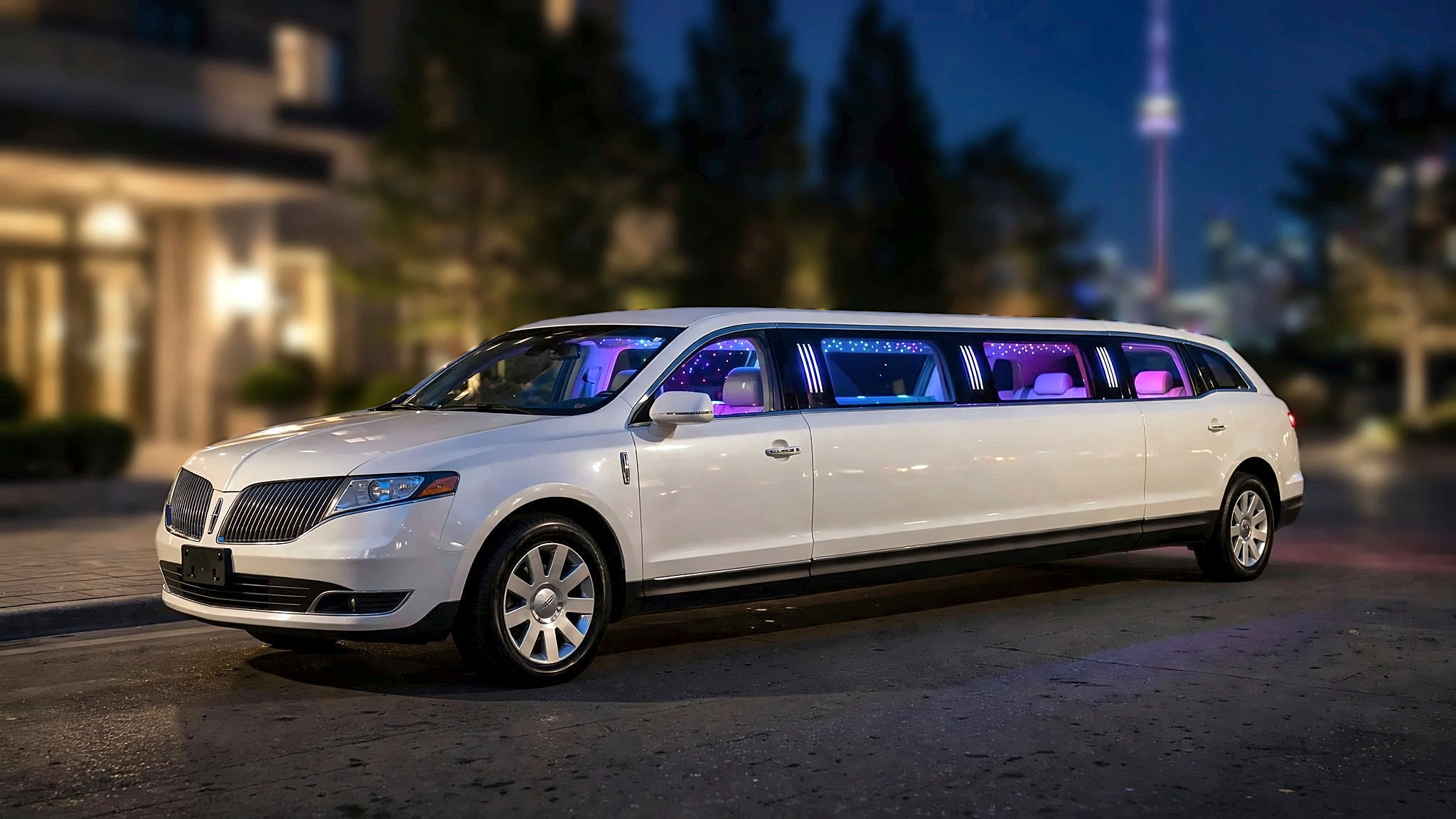 The white Lincoln MKT stretch limousine in downtown Toronto at night, with the CN Tower behind