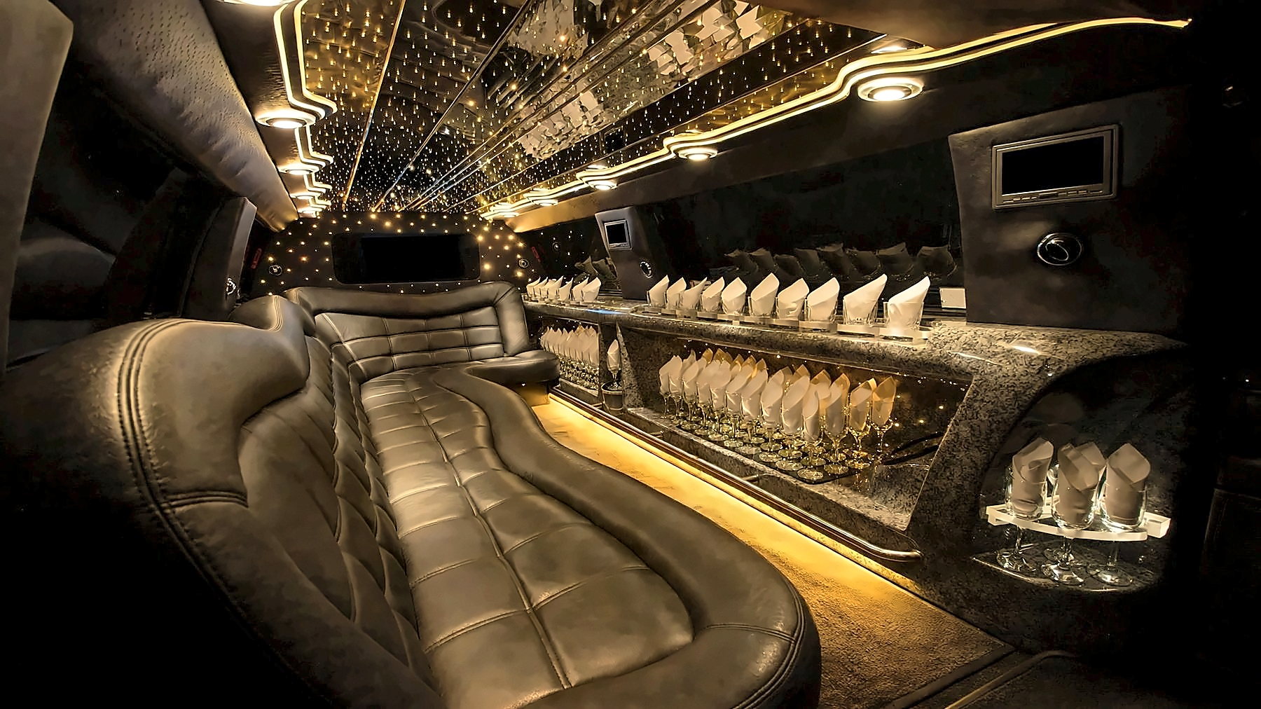 Interior of the 12-passenger Lincoln Navigator Stretch Limousine with leather seating, a lit bar area and gold cabin lighting