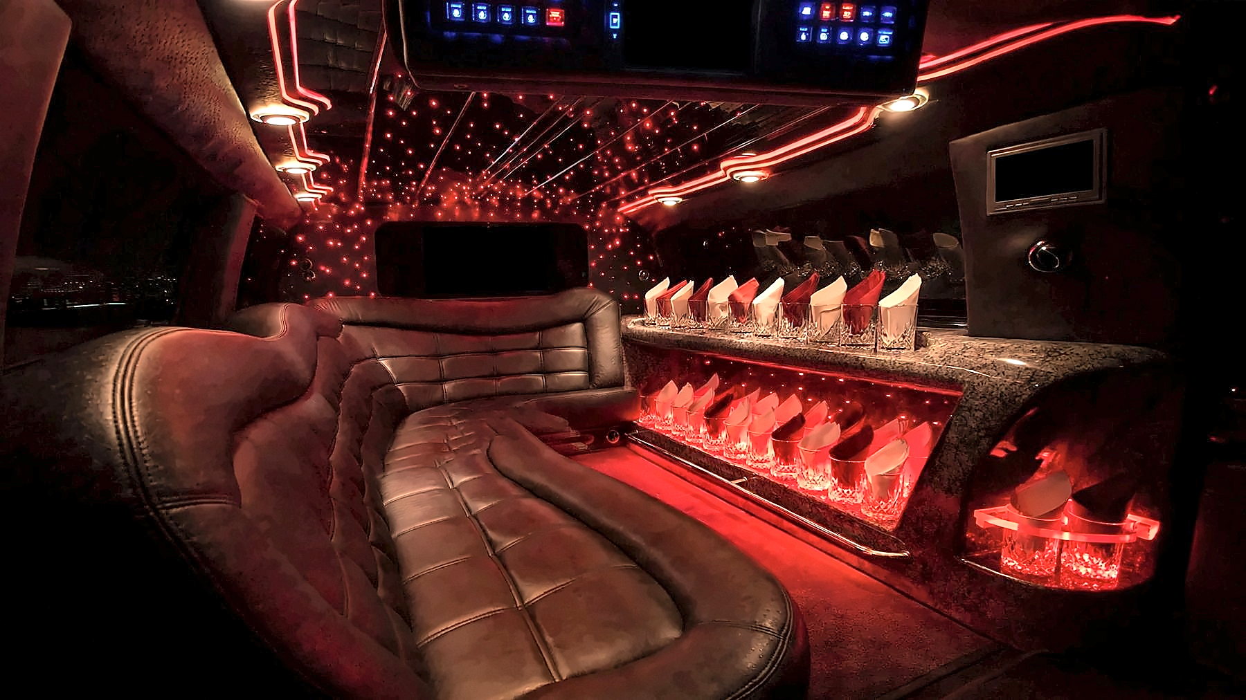 Interior of the 12-passenger Lincoln Navigator Stretch Limousine with leather seating, a bar area with glassware and red cabin lighting