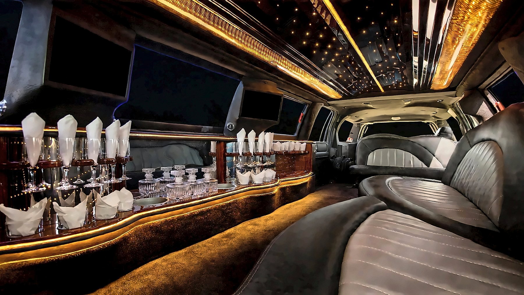 Interior of the Lincoln Navigator Stretch with leather seating, a bar with glassware and amber starlight ceiling lighting