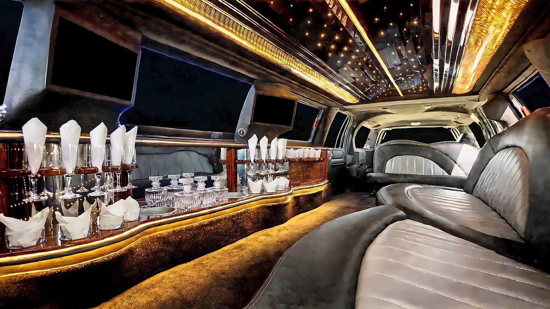 Interior of the Lincoln Navigator Stretch with leather seating, a bar with glassware and amber starlight ceiling lighting