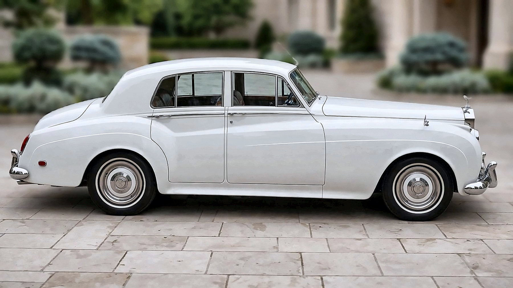 The white 1959 Rolls-Royce in side profile at an estate entrance