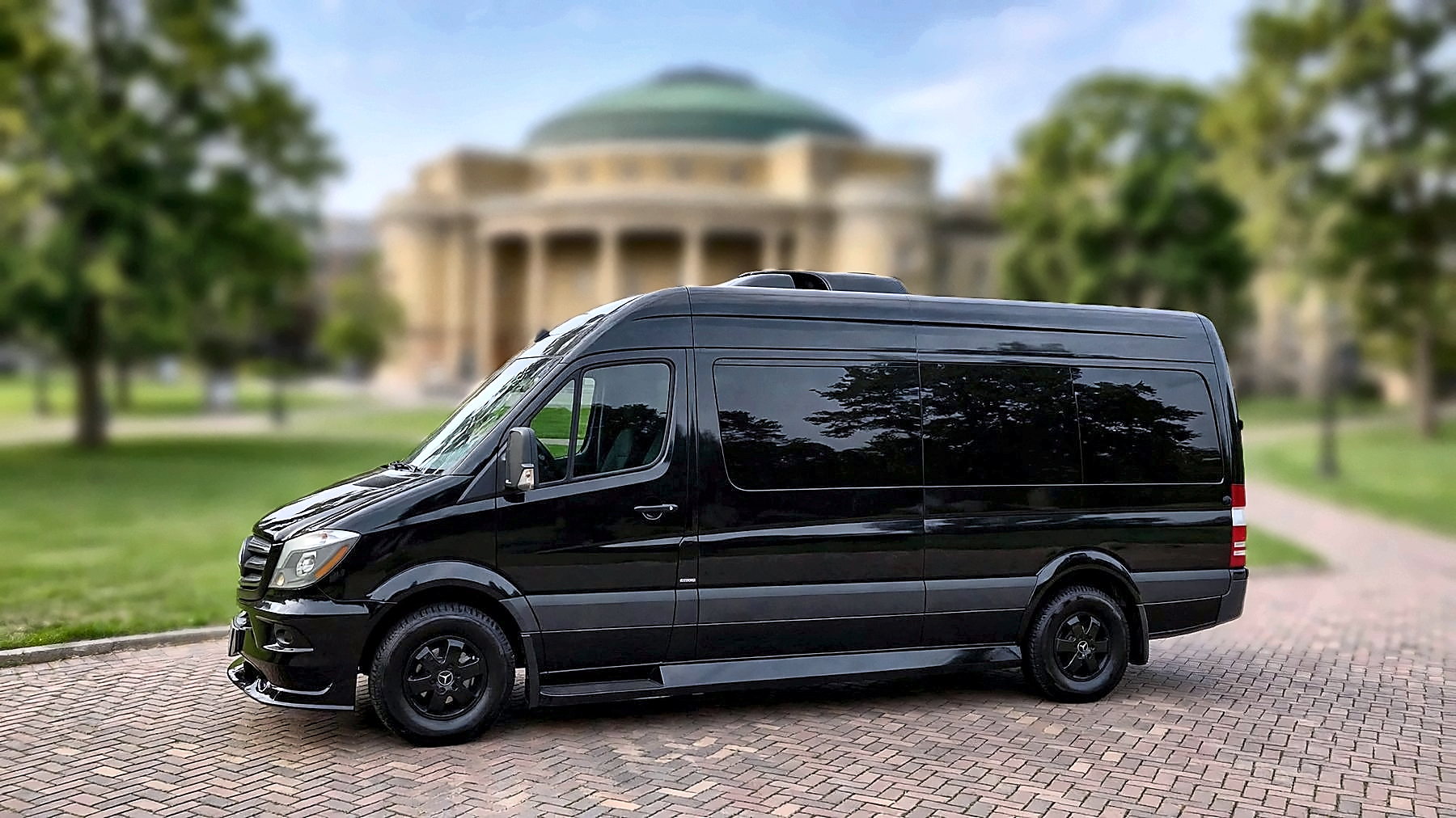The black Mercedes-Benz Sprinter in side profile on a university campus